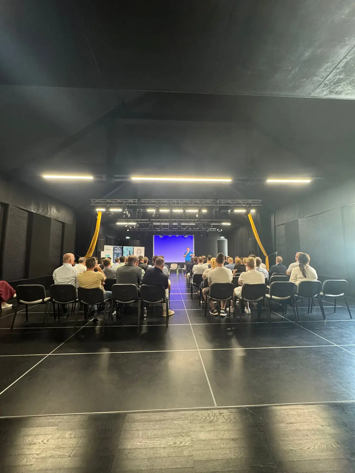A full hall during the presentation — attendees and a speaker on stage.